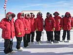 Congressional members wearing matching red polar parkas pose for a picture at the South Pole. 