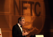 Gutierrez on podium with large NFTC logo in background. Click for larger image.