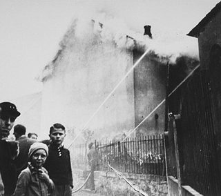 As the synagogue in Oberramstadt burns during Kristallnacht (the "Night of Broken Glass"), firefighters instead save a nearby house. Local residents watch as the synagogue is destroyed. Oberramstadt, Germany, November 9-10, 1938.