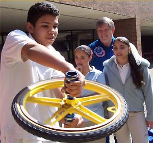 Two students and astronaut Roger Crouch watch as another student spins a bicycle wheel gyroscope.