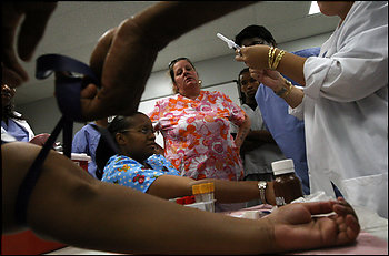 Phlebotomy instructor Shelly Chasteen, above center, watches as her students prepare to do blood draws in the Sanz College 12-week program. Student Theresa Reed, left, takes blood from the finger of one of her peers. After 92 hours of training, the students should have completed 42 successful venipunctures.
