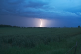 single bolt of lightning behind open field at night sky