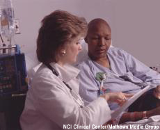 Photograph of a female health professional at the bedside of a bald female chemotherapy patient