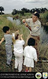 photo of Service employee showing wetlands critter to children.  Titled:  Environmental Education