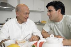 Fotografía de un hombre mayor y un joven hablando mientras desayunan