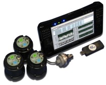 Photo showing a grouping of objects, including three sensors that are circular in shape and black in color with metal affixed to the top of each; a USB device; and a flat computer screen depicting measurements.
