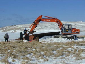 An excavator removes a rusted barge on a sunny winter day on St. Paul Island, Alaska