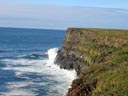 On a sunny day, the waves of the Bering Sea break against the base of tall cliffs