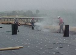 Figure 1. Workers applying hot asphalt to fiberglass felt (on a roof).