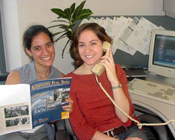 Two women smiling; one is talking on the phone while the other reads.