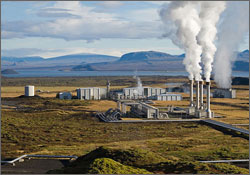 A photo showing the Nesjavellir Geothermal Power Plant situated on the open plains of Iceland, with steam venting from stacks and piping to carry hydrothermal water and steam to and from the plant.