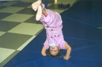Photo of young girl with a below the elbow amputation (right arm), performing a headstand on a mat.
