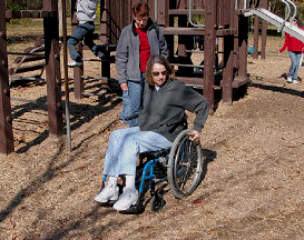 Photo of a person using a wheelchair testing out treated engineered wood fiber at a playground.