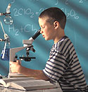 A boy in a class room looking into a microscope.