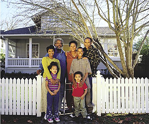 A family standing outside their house and white picket fence.