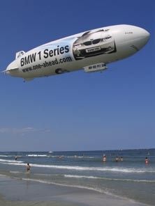 A blimp floats over a crowded beach.