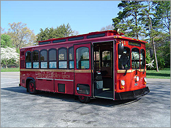 Photo of a bright red trolley moving down a tree-lined street with Knoxville Trolley Lines painted in gold on its side underneath the windows.