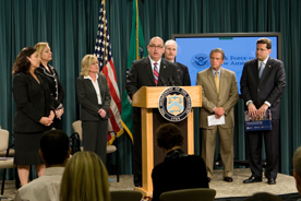 task force members surroundingUSCIS Director Emilio Gonzalez as he speaks from the podium