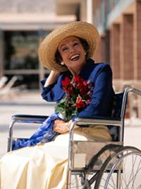 Happy, smiling woman sits in a wheechair holding a bouquet of roses