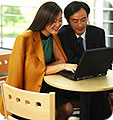 A man and woman looking at a laptop monitor.