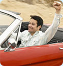 A man driving a red convertible with his fist up in the air celebrating.