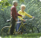 A man and a woman riding their bikes through a park.