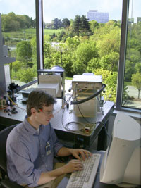 Physicist Joshua Bienfang sets up the NIST quantum key distribution system to receive a string of photons from colleagues stationed on the top floor of the NIST Administration Building (shown in the background.) The black instrument on the left is an 8-inch telescope used in collecting the incoming photons. Photo by Gail Porter/NIST