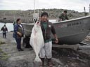 A St. George resident stands in front of a small fishing boat proudly holding a halibut.