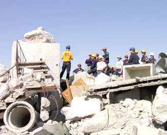 first responders in hard hats stand on a pile of concrete rubble
