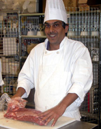 A MBEPB student wearing a chef's hat and cutting meat. 