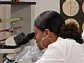 Student looks into microscope as other students in lab look on.