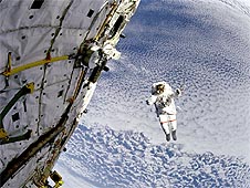 Lee in a spacesuit in front of Earth, with the shuttle in the foreground