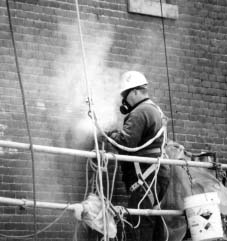 Worker in a cloud of dust on a scaffolding next to a brick wall