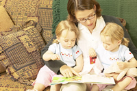 Photo of young twins reading a book with their mother