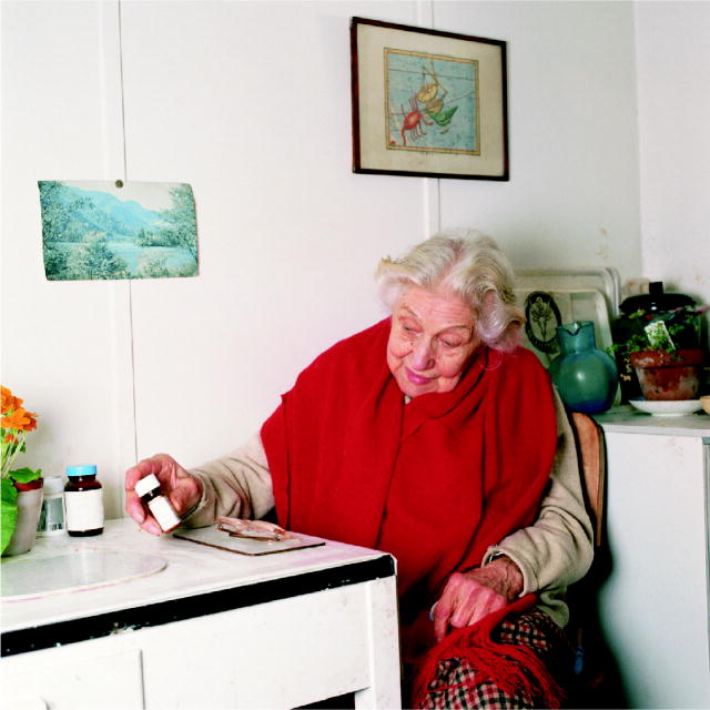 This photo shows an elderly woman looking at a bottle of prescription medicines.