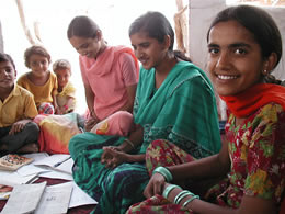 Photo of three adolescent students in a village near Jodhpur, India, sitting during an English lesson while younger children listen in.