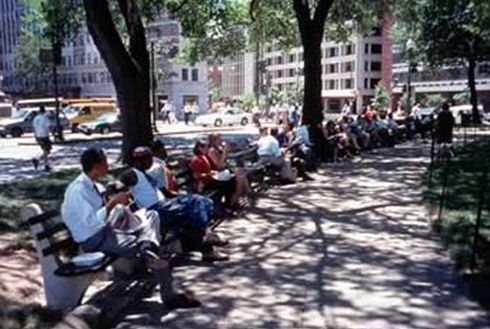 The picture on the left shows benches placed at the back of the sidewalk, with nearly all benches being used by people. 