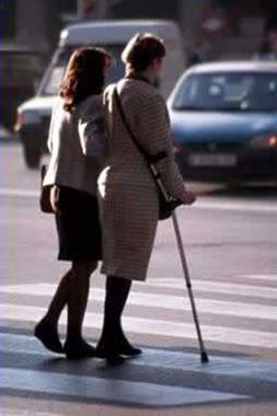 The second picture on the right of the slide shows a woman with an arm-braced cane crossing a street with the assistance of another adult.