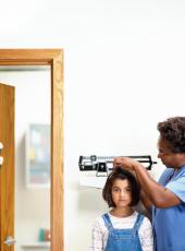 Photograph of a female nurse measuring a young girl's height