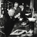 image of Thomas Edison in his laboratory with two onlookers