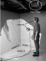 Figure 1: The NIST immersive visualization system.  A single
    3D scene is being displayed across the three screens. Note the tracker transmitter, a tracker sensor on the user's stereo glasses, and another
    sensor on a hand-held pointing device.