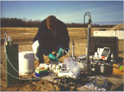 A technician is pumping water from a multi-level well during an investigation of the natural attenuation of a chlorinated solvent plume under a fire training pit. Tubing from the well leads to an in-line multi-parameter probe that records pH, dissolved oxygen, Eh, and temperature