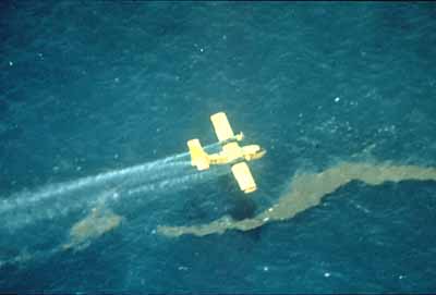 Aerial view of airplane spraying dispersant on oil slick on water.