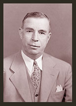 A black and white portrait of Senator Dennis Chavez, who is wearing a dark jacket, white shirt, and a striped tie.