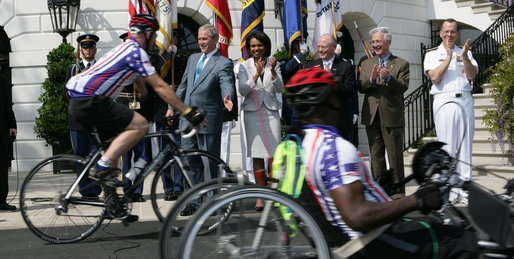 President George W. Bush reaches out to participants of the Wounded Warriors Soldier Ride as they cross in front of him during the kickoff Thursday of the White House to Lighthouse ride. White House photo by Chris Greenberg