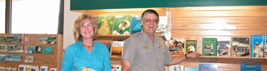 A female Eastern National employee dressed in an aqua colored blouse stands next to a male park ranger at the Naval Live Oaks bookstore.