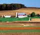 Farmstead with rows of crops in foreground and barn with silo in background.