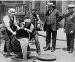 Deputy Police Commissioner John A. Leach, right, full-length portrait, standing, facing right, watching agents pour liquor into sewer following a raid during the height of prohibition.  LC-USZ62-123257