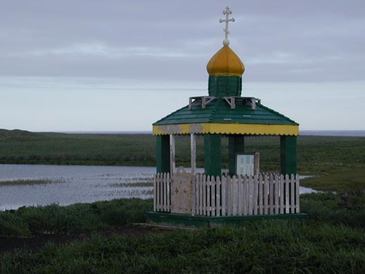 A green, yellow and white wooden shrine sits in front of a small lake at Northeast Point.  A traditional white Russian Orthodox cross sits atop the roof.