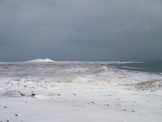 Snow-covered tundra and dune hills, with a taller volcanic cone in the background